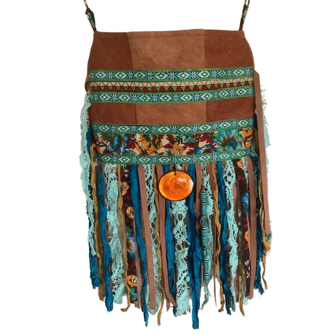 Handmade boho phone bag with floral print, green geometric ribbon, layered fringe in teal and brown, and orange glass pendant detail