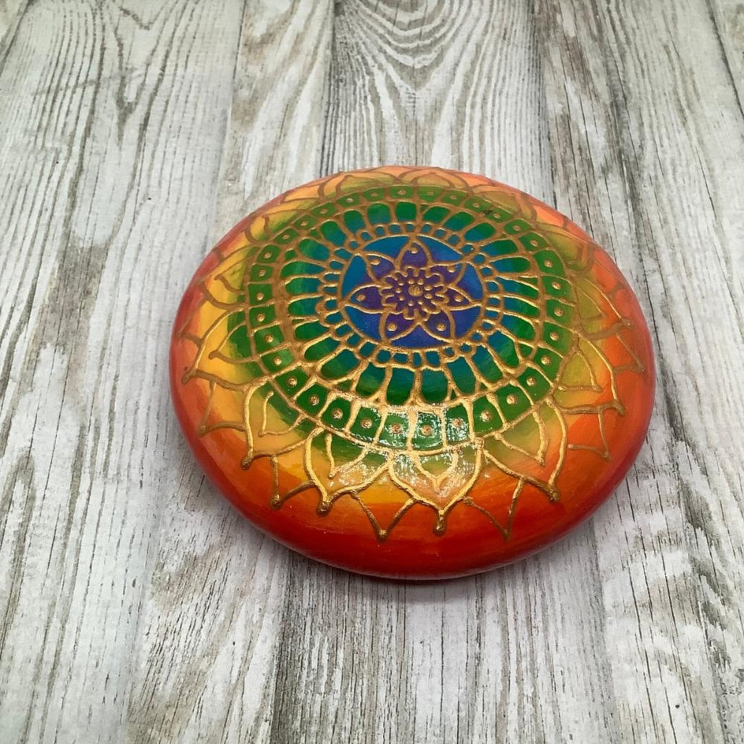 Close-up of a hand-painted mandala stone in rainbow colors with a high-gloss finish.