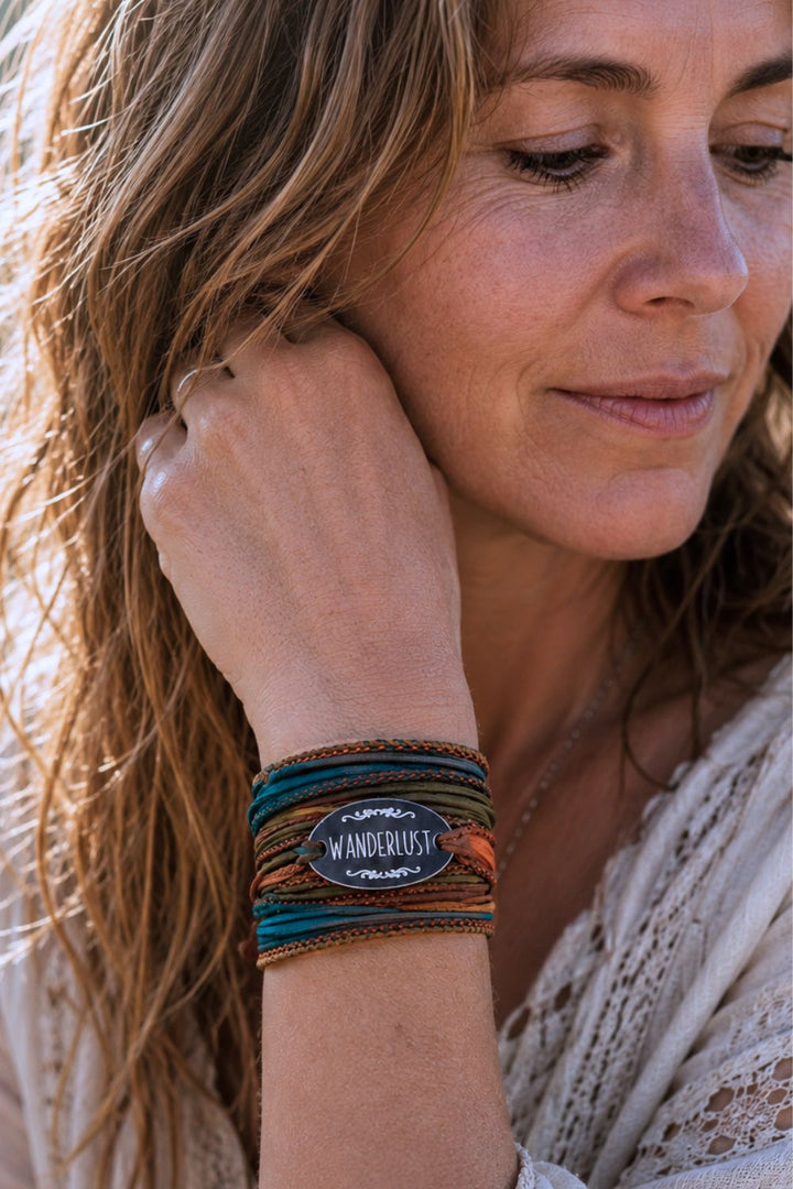 Woman wearing a handmade Wanderlust silk wrap bracelet in earthy teal and copper colors. Boho jewelry for travel fashion, festival style and everyday adventures, photographed in natural golden hour light.