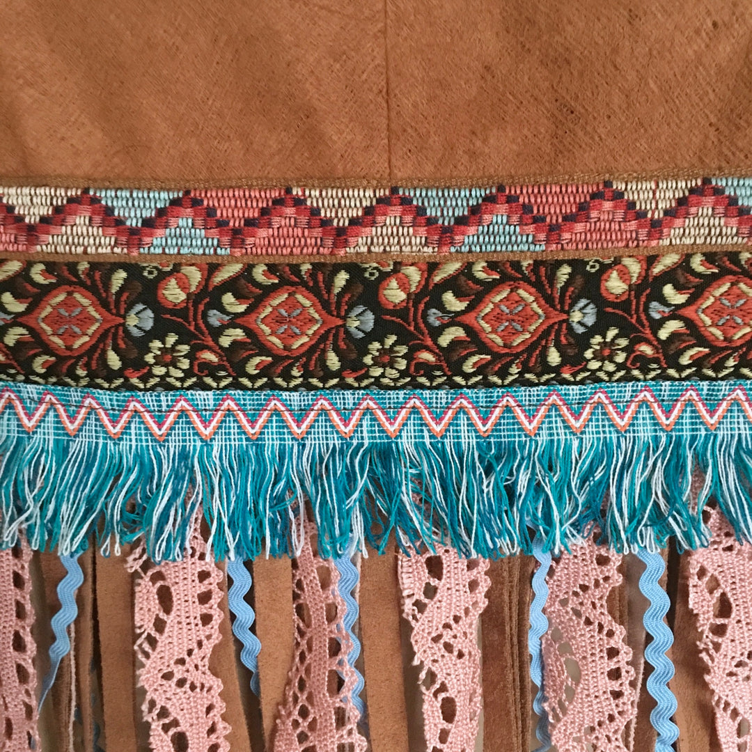 Close-up of decorative fabric with intricate patterns and fringes on a brown background