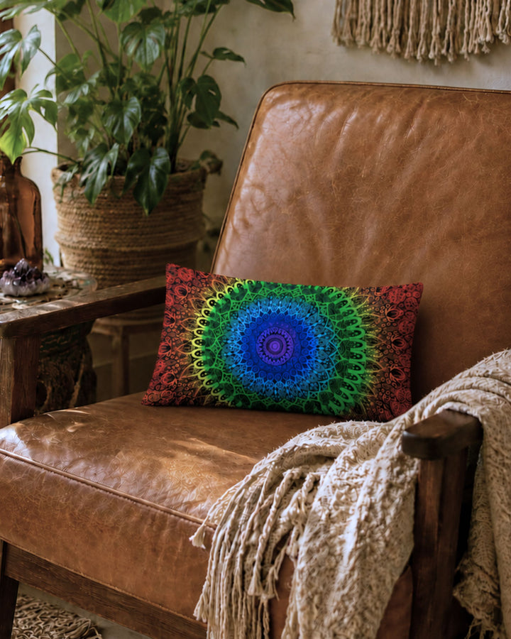 Rainbow chakra mandala lumbar pillow on a vintage cognac leather armchair in a warm bohemian interior with macramé wall hanging, tropical plants, cozy neutral blanket and soft golden natural light.