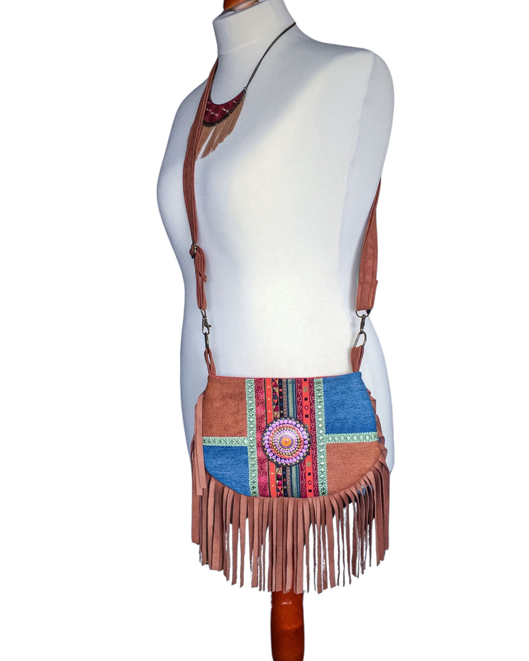 Brown barkcloth crossbody bag with colorful pattern and fringes on a mannequin.