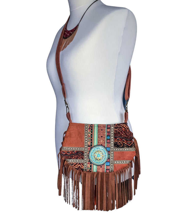 Brown barkcloth crossbody bag with fringe and decorative elements on a mannequin.