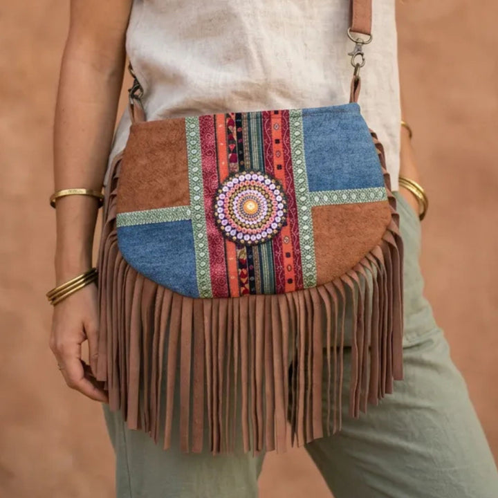 Colorful fringed handbag with patterned strap held by a person against a brown background