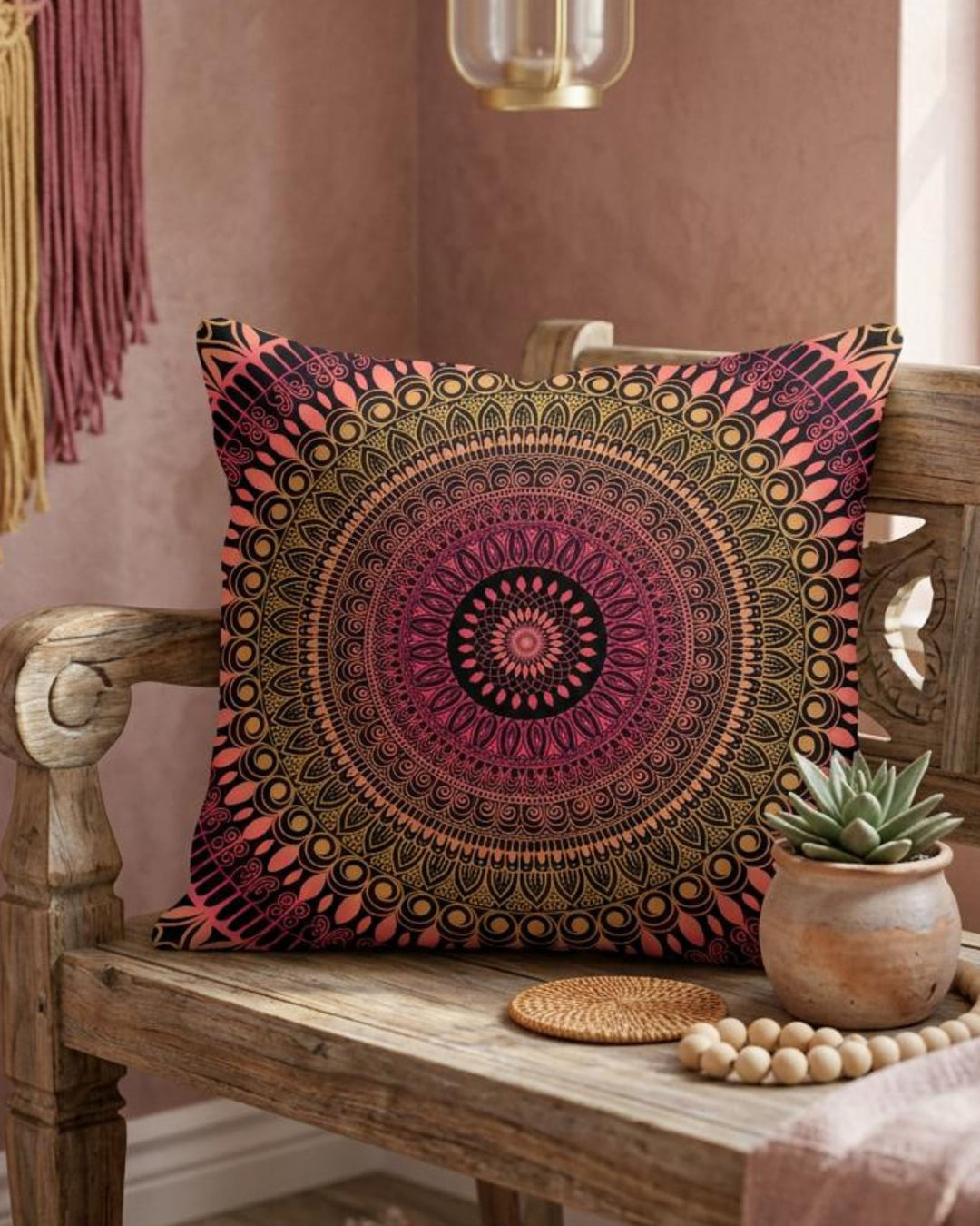 Boho square pillow cover in pink, coral, gold and black mandala design styled on a rustic wooden bench in a warm colorful boho interior
