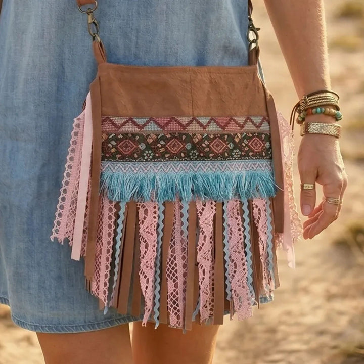 Boho crossbody bag made of bark cloth with blue and pink details and fringe, styled with a denim dress and boho jewelry in a warm golden field setting.