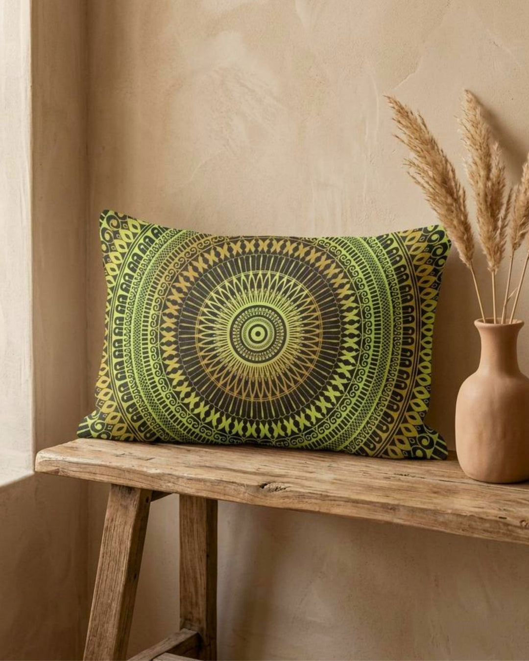 Boho lumbar pillow cover with green and yellow mandala design on a rustic wooden bench, styled with a ceramic vase and dried pampas grass, warm natural light and textured beige wall, premium linen-look fabric