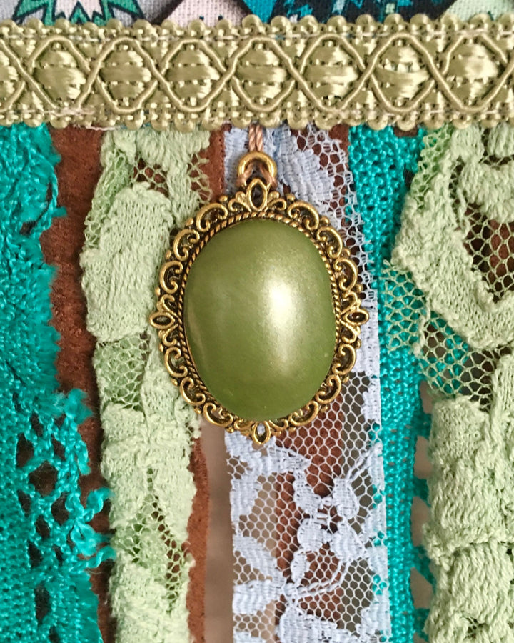 Decorative brooch with a green gemstone and gold frame on a textured fabric background