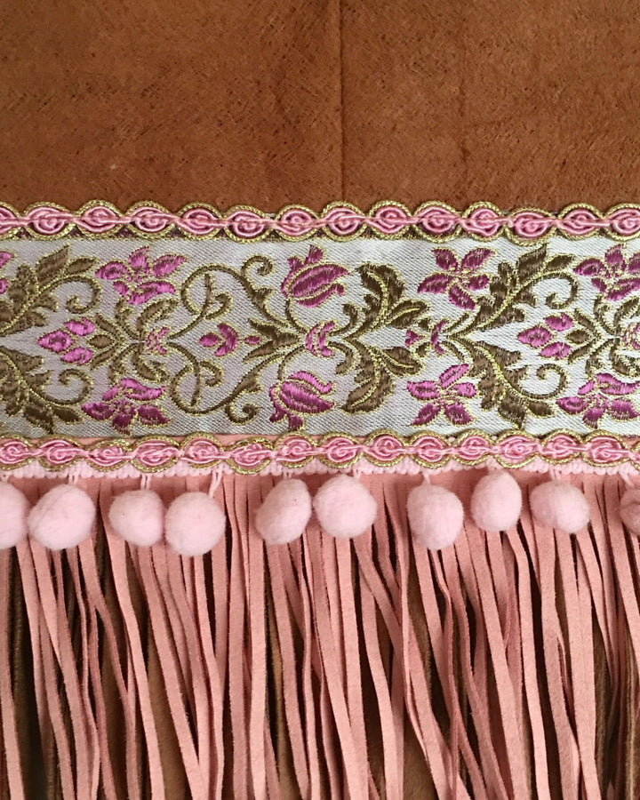 Decorative trim with floral pattern and pink tassels on a wooden background