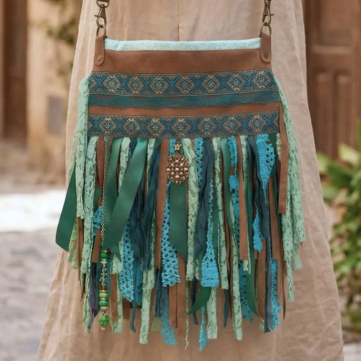 Close-up of a handmade upcycled bohemian crossbody bag in turquoise and green tones with lace, ribbon and fringe details, showing rich textures and layered fabrics