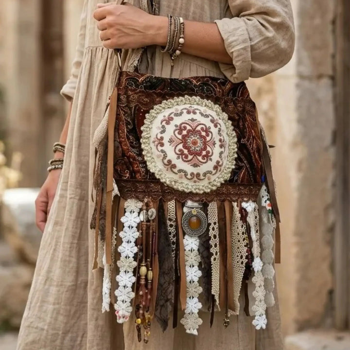 Decorative handbag with intricate patterns and fringes held by a person in a beige outfit.