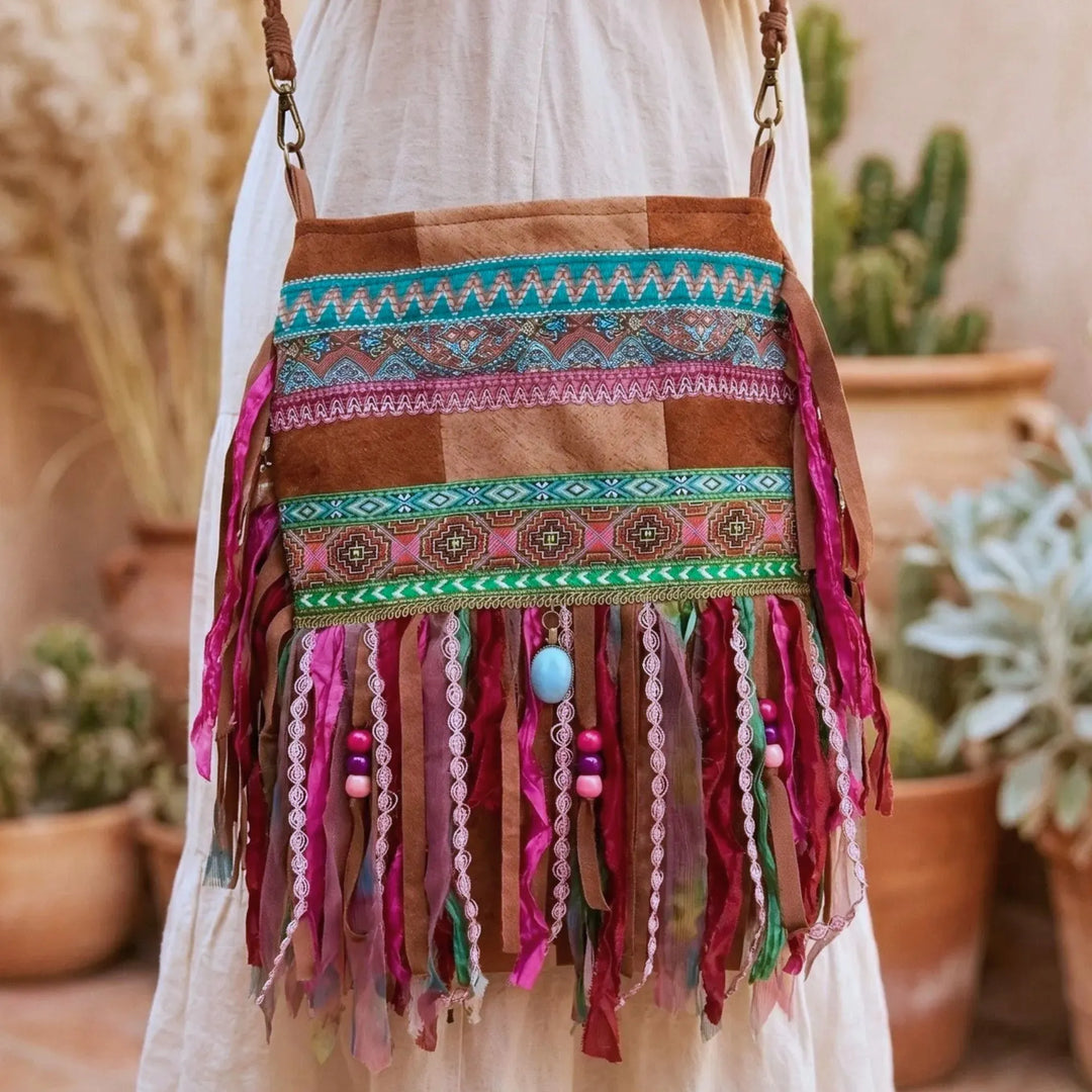 Bohemian handgemaakte crossbody tas met kleurrijke franjes, kralen en etnische patronen, gedragen op heuphoogte bij een lichte linnen jurk in een warme mediterrane setting
