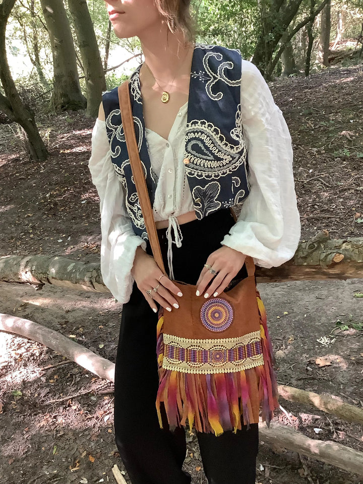Woman holding a brown handbag with colorful fringe in a forest setting
