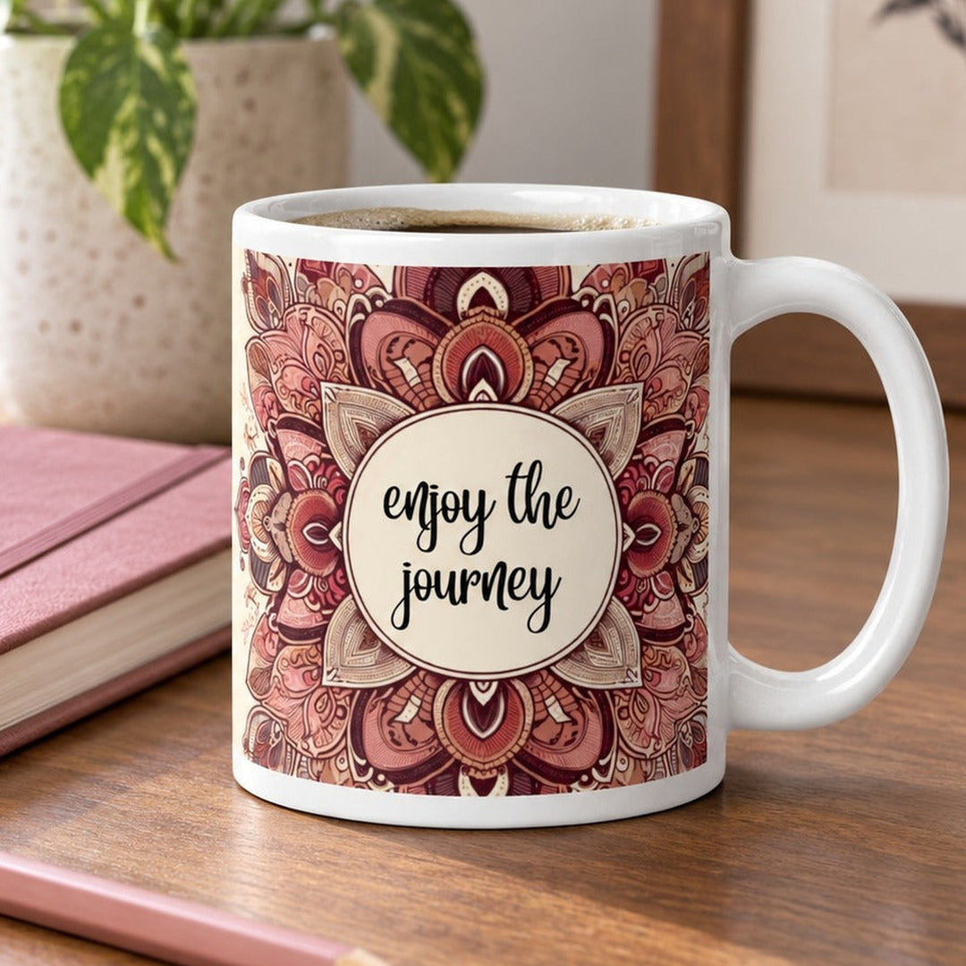 Close-up lifestyle photo of white ceramic Enjoy the Journey mug with pink mandala design.
