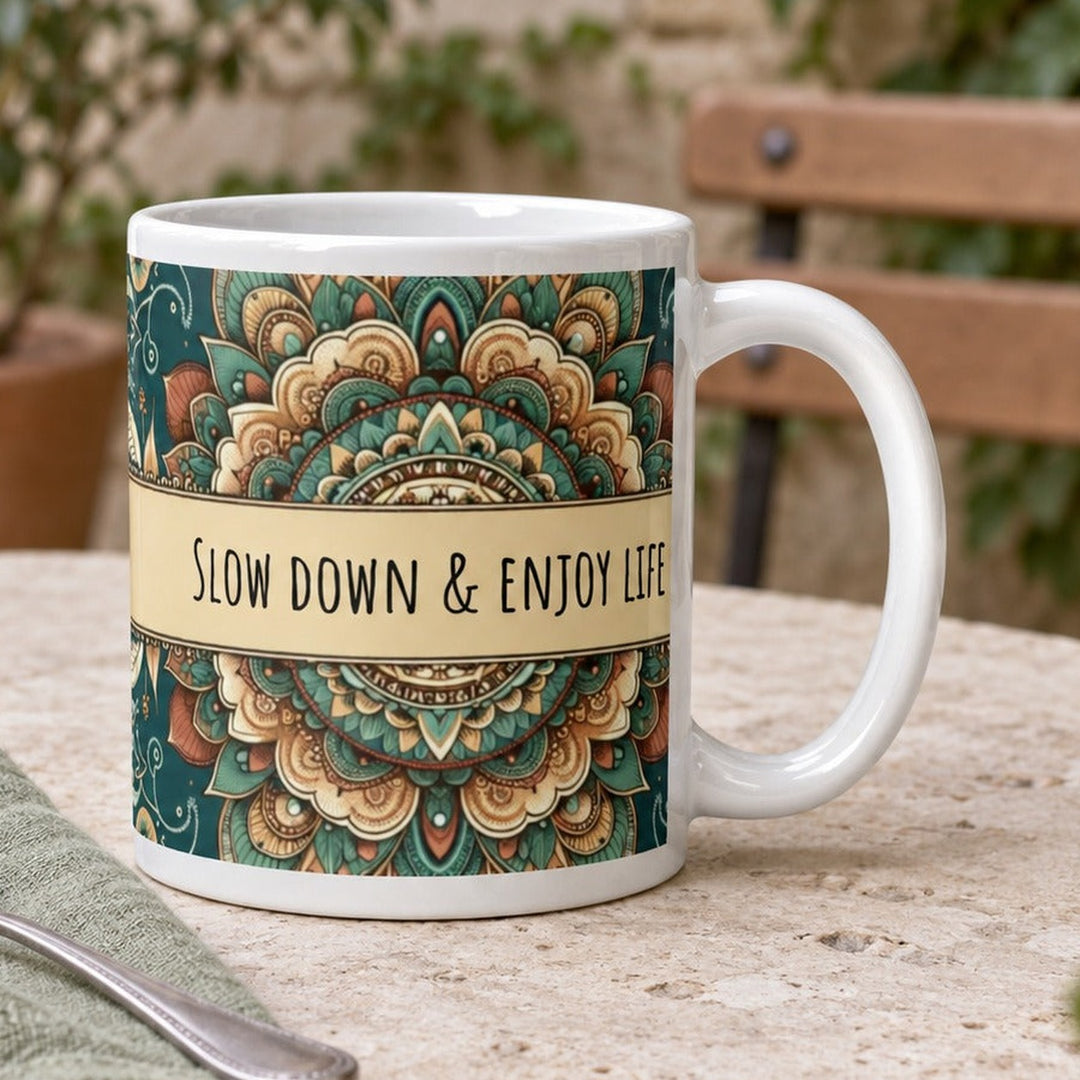 Close-up lifestyle photo of white ceramic Slow Down and Enjoy Life mug with mandala design.
