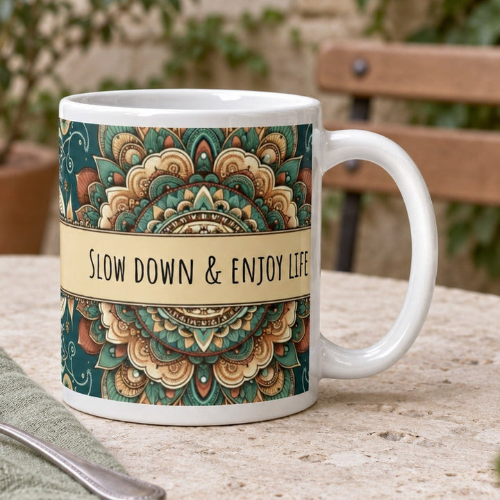 Close-up lifestyle photo of white ceramic Slow Down and Enjoy Life mug with mandala design.