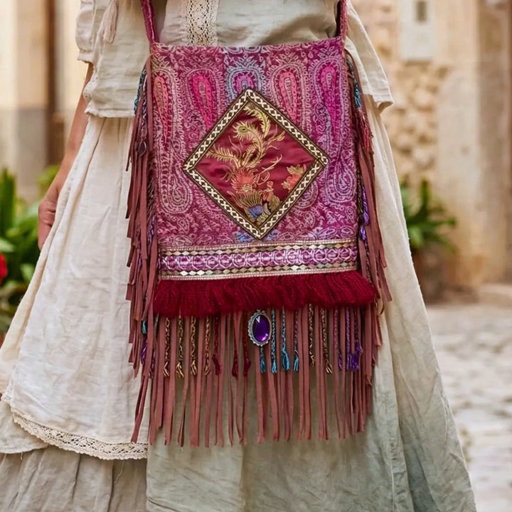 Decorative handbag with fringes and intricate patterns worn by a person in a light-colored outfit.