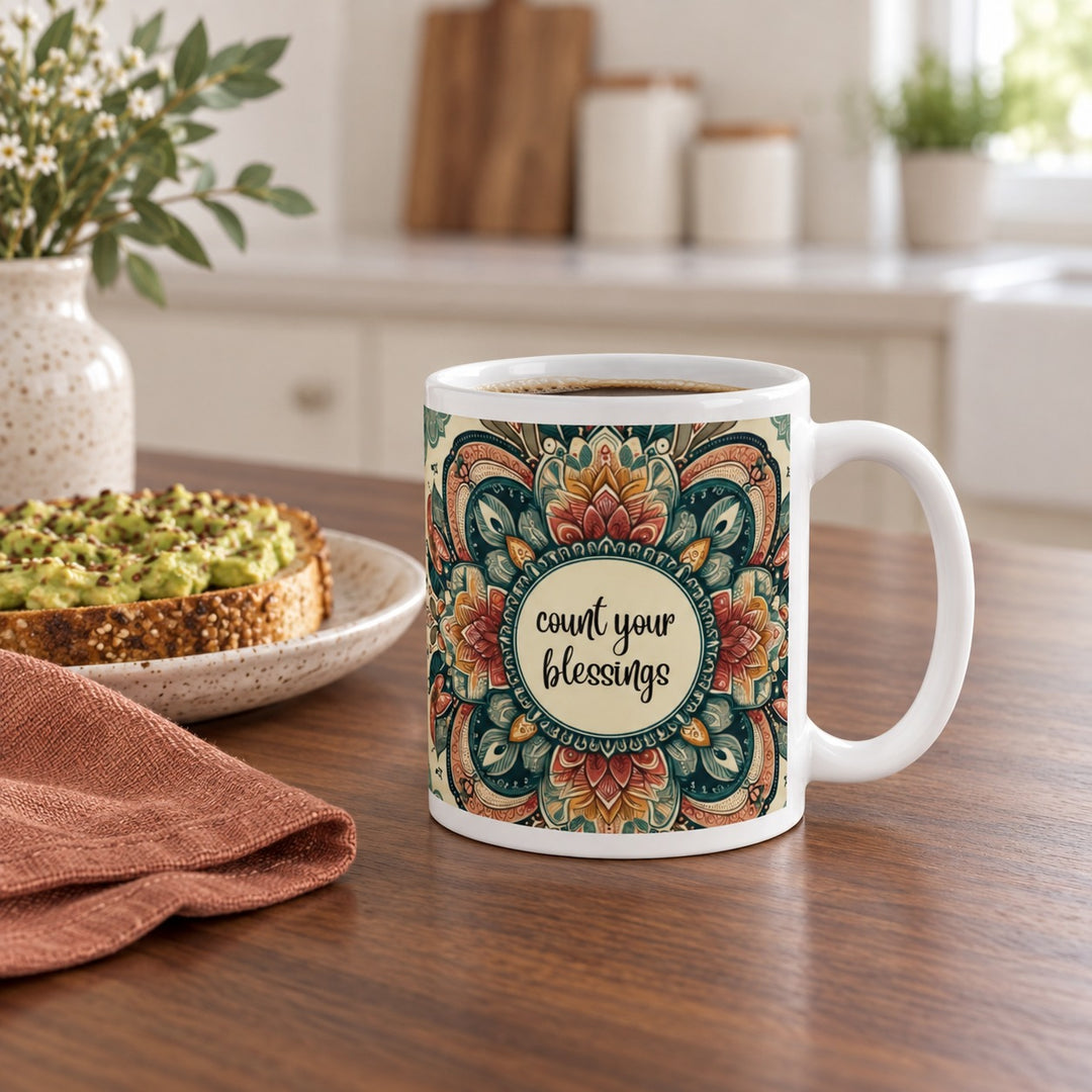 11 oz Count Your Blessings mug with a green and rust mandala on a breakfast table beside toast.