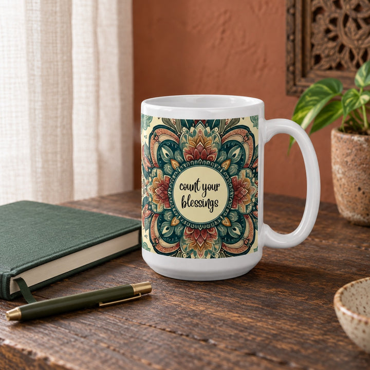 15 oz Count Your Blessings mandala mug on a wooden desk beside a green journal and pen.