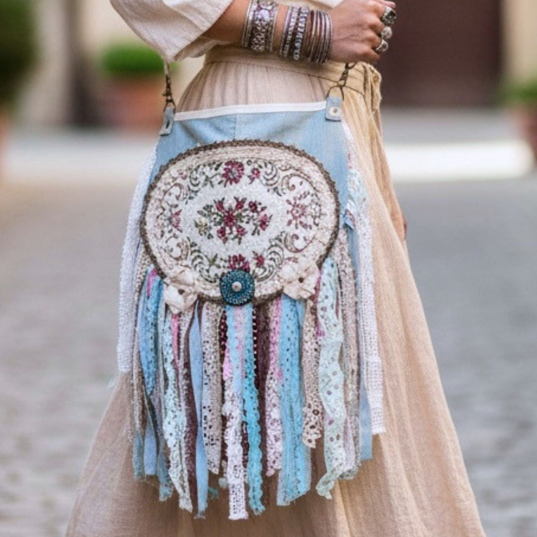 Handmade boho crossbody bag with pastel fabrics, lace, embroidery and fringe details, worn with a neutral linen dress, detailed view of textures and craftsmanship