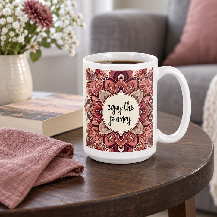 15 oz Enjoy the Journey pink mandala mug on a wooden table beside a book and dusty rose linen.