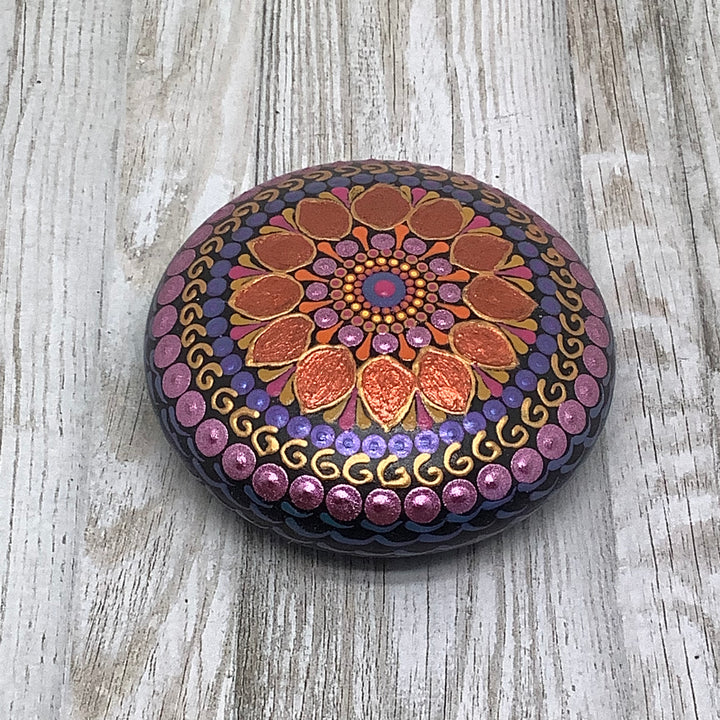een kleine mandala steen in oranje, paars en roze