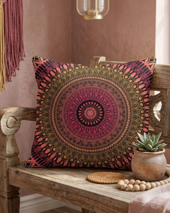 Boho square pillow cover in pink, coral, gold and black mandala design styled on a rustic wooden bench in a warm colorful boho interior
