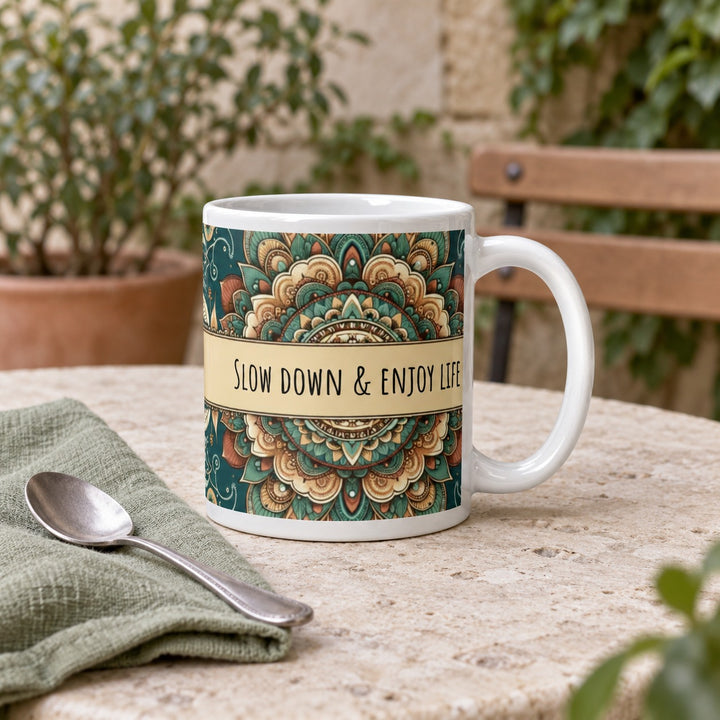 11 oz Slow Down & Enjoy Life green mandala mug on a stone courtyard table beside a sage napkin.