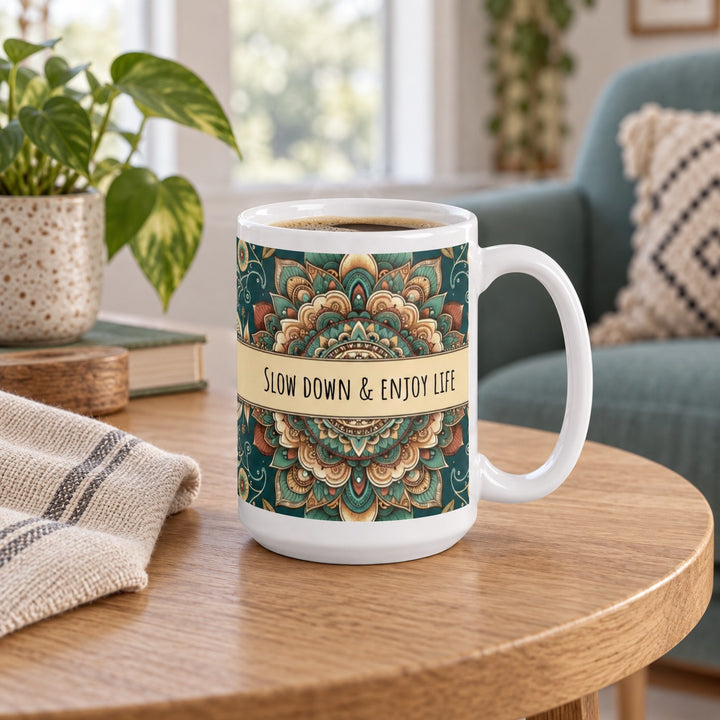 15 oz Slow Down & Enjoy Life mandala mug on an oak side table beside a teal armchair.