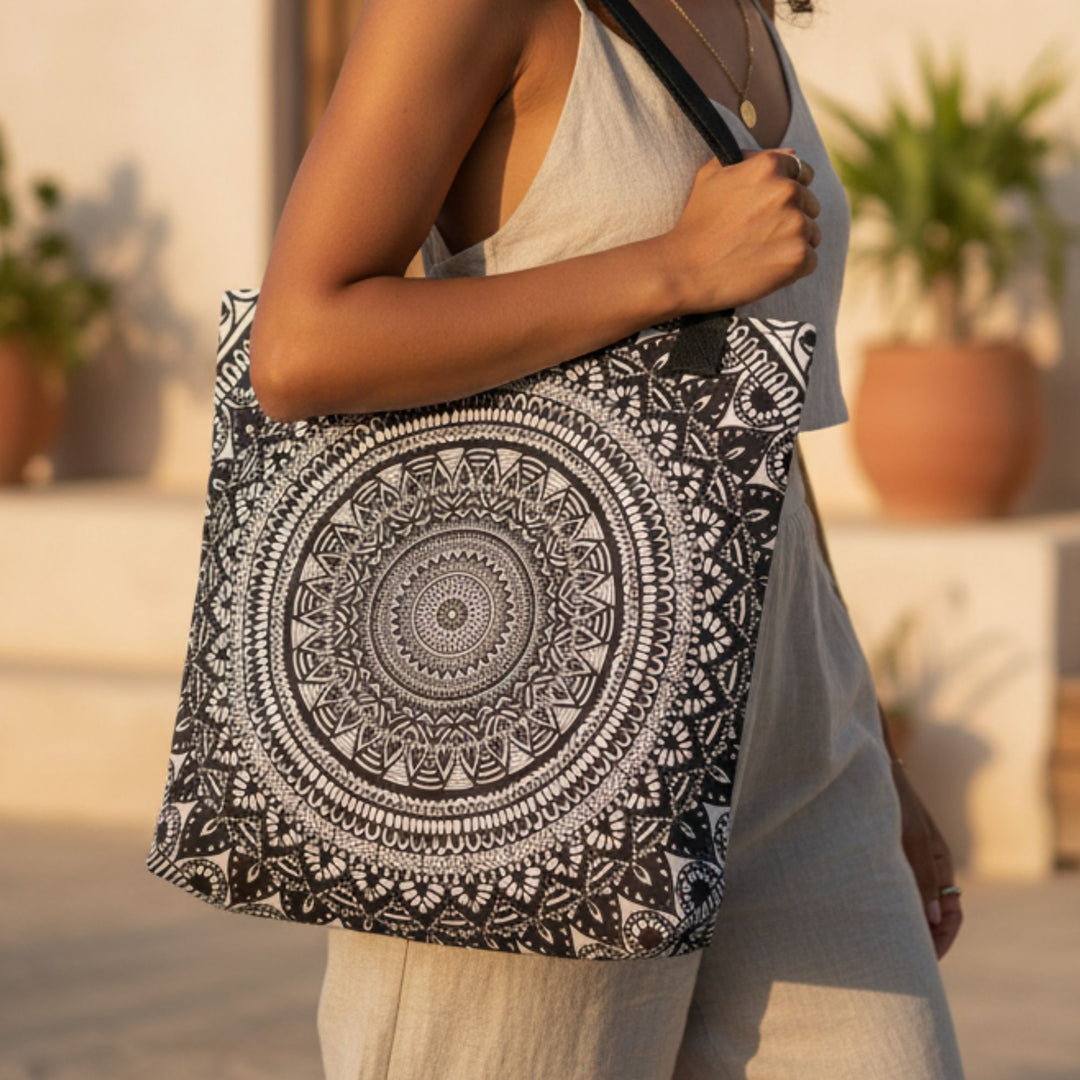 close-up of black and white mandala tote bag with detailed geometric pattern, worn over shoulder in warm golden sunlight, bohemian style