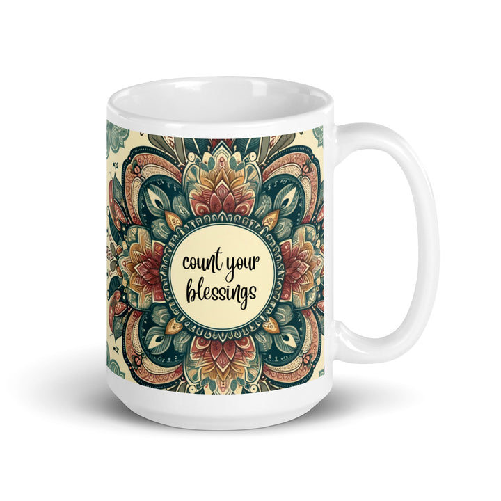 White ceramic mug with a detailed green, red, and gold mandala design and the phrase 'Count Your Blessings' in the center.