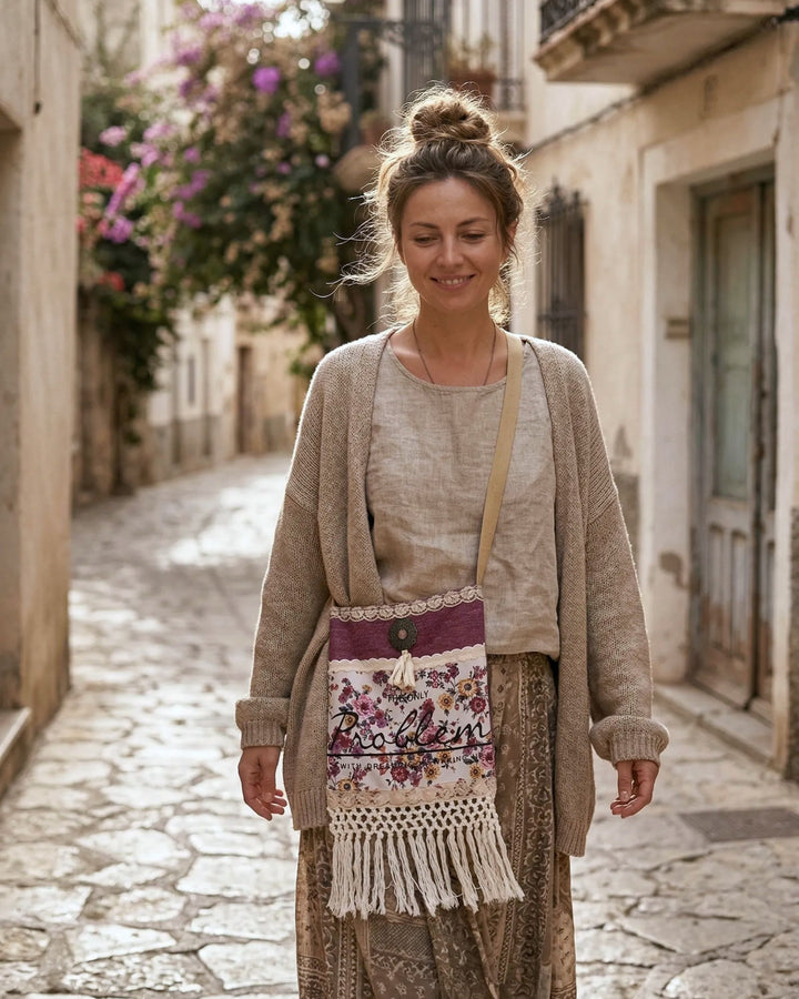 Vrouw in boho outfit met handgemaakte crossbody tas met bloemenprint en ecru franjes, gedragen in een zonnige mediterrane straat met warme natuurlijke tinten